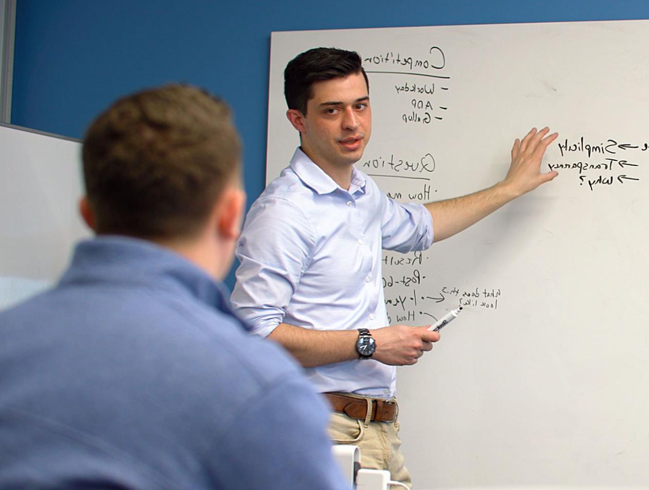 Student at white board explaining marketing plan to client.