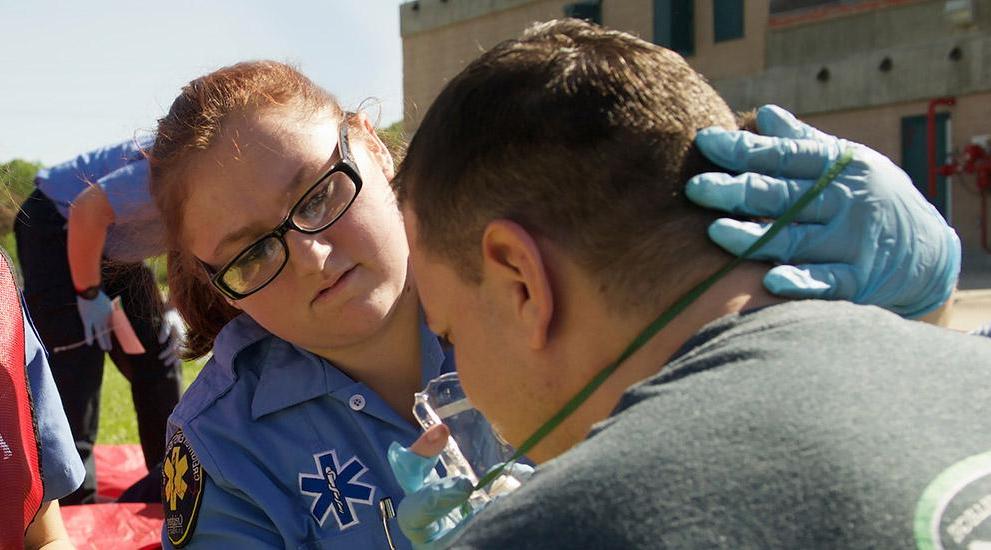 A female EMS student assists a man with an oxygen mask